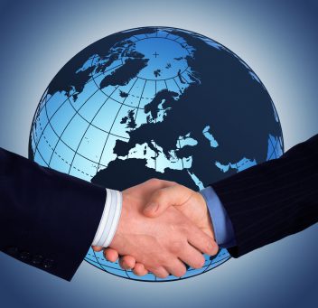 two people wearing suits shaking hands in front of a globe.