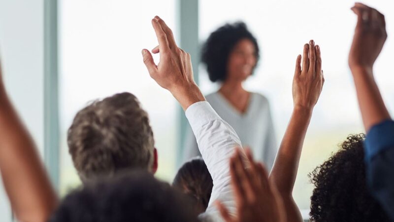 A group of people raise their hands to ask questions during a presentation.