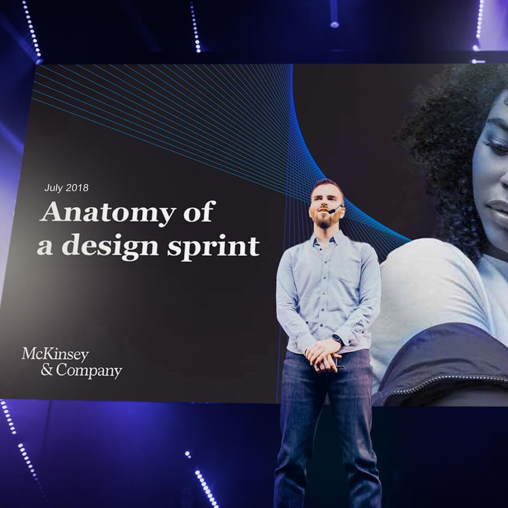 A man on a stage leads a presentation on Anatomy of a design sprint.