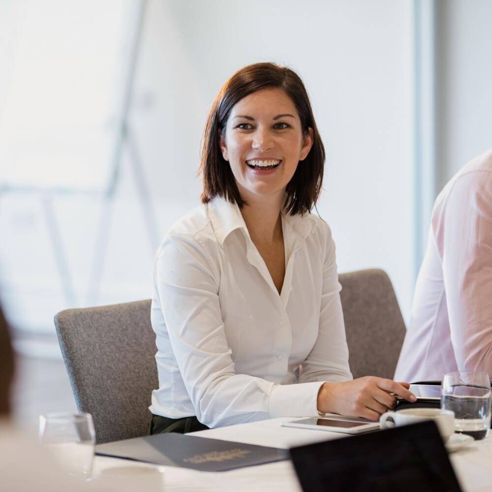 A woman smiles while sitting at a conference room table.