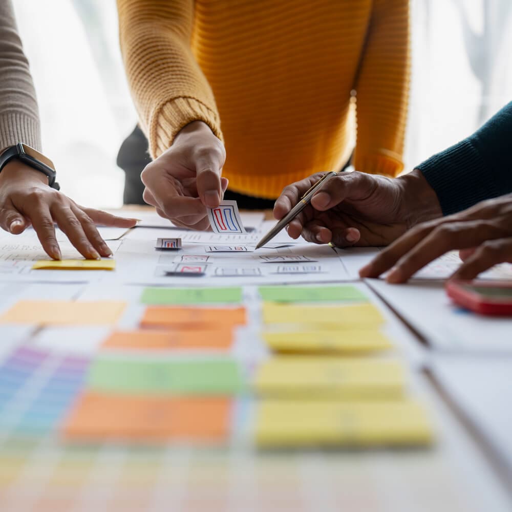 A group of people point at a project on a tablet, with colorful sticky notes.