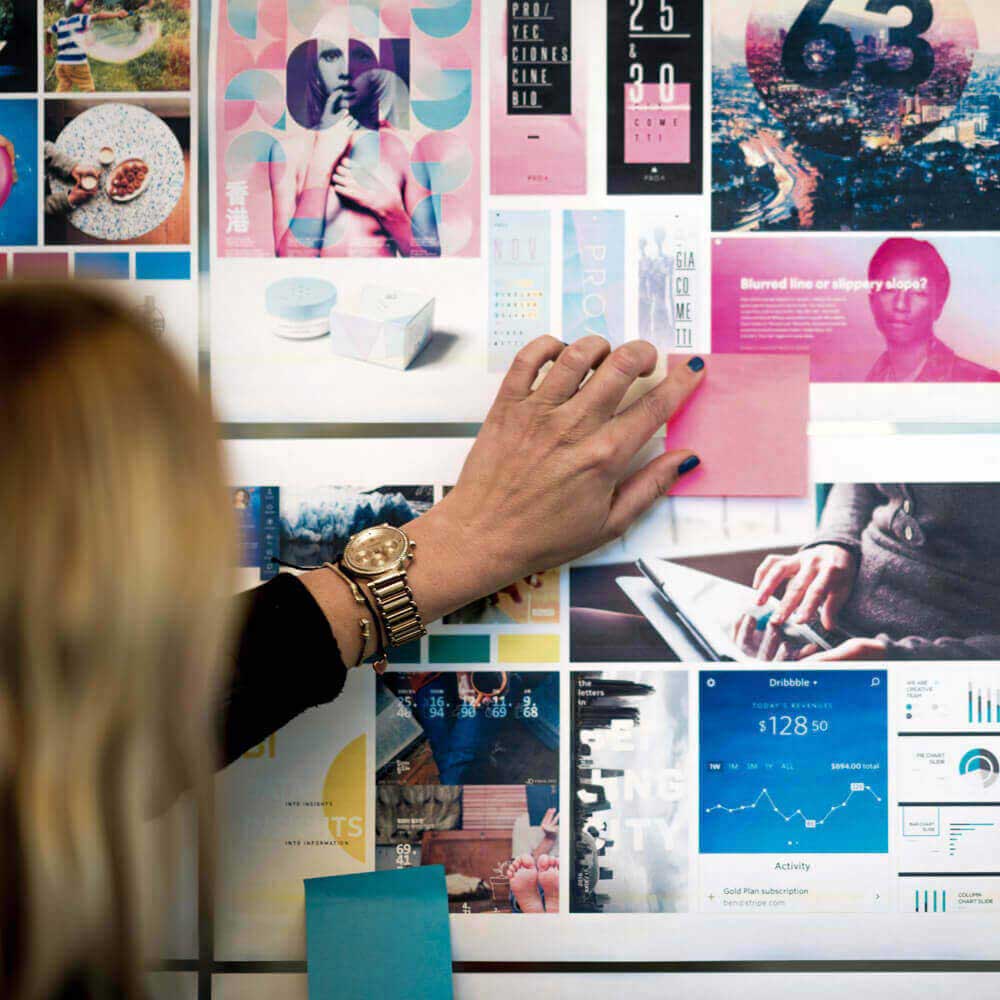A woman points at a vision board with images, slides, and sticky notes.