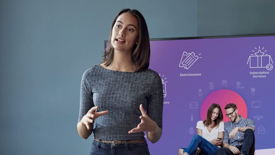 A woman leads a talk while in front a presentation screen.