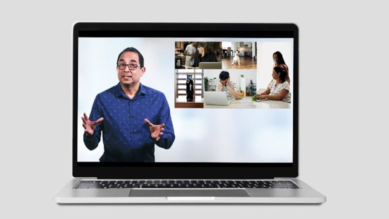 A laptop screen shows a man leading a presentation.