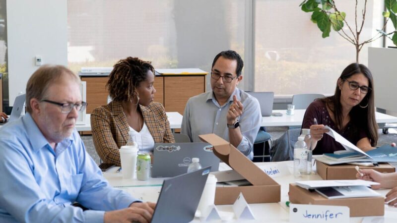 A team of people sit in a conference room and make plans on their laptops.