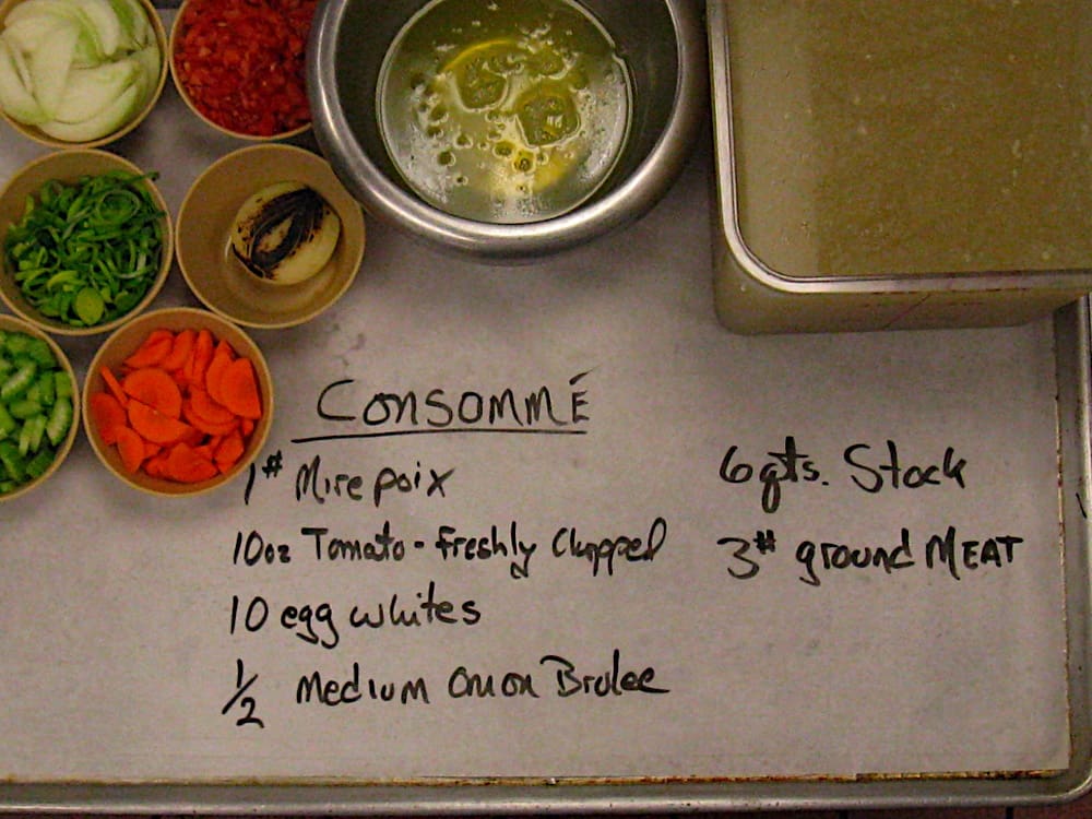 Ingredients on a baking sheet lined with parchment paper. Ingredients to make consomme are written on it