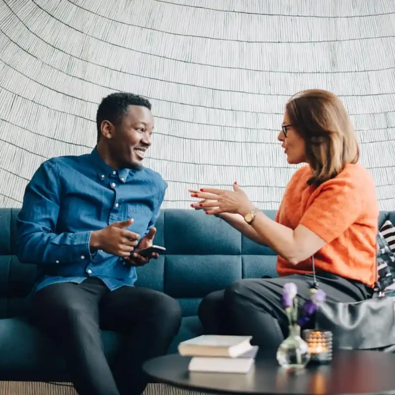 Two people on a blue couch are talking.