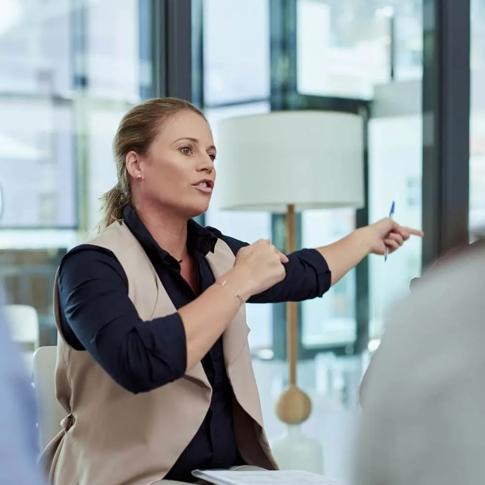 A woman is talking and pointing her hands in a conference room.